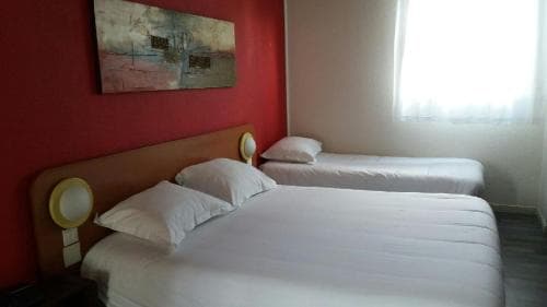 A cozy hotel room features two neatly made beds against a vibrant red wall adorned with abstract art, creating a warm and inviting atmosphere ideal for travelers seeking comfort and relaxation.