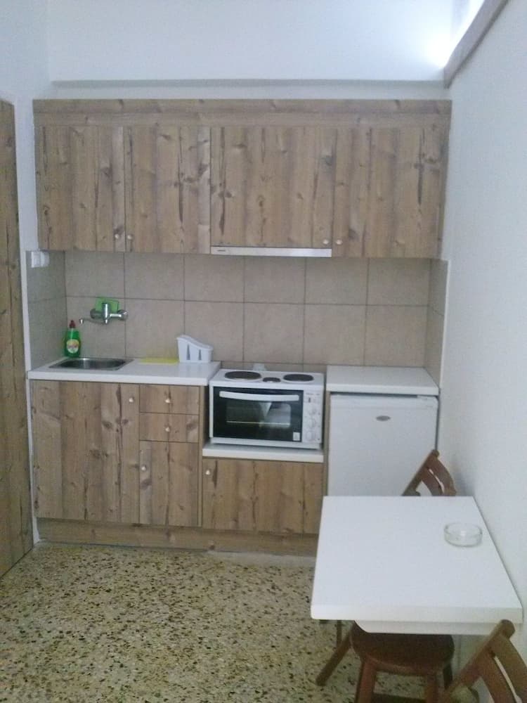 A cozy, rustic kitchenette with wooden cabinets and tiled backsplash offers a simple dining setup with a white table and chairs, ideal for travelers seeking self-catering accommodations.
