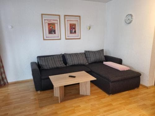 A cozy living room with a dark gray sectional sofa, wooden coffee table, framed artwork on white walls, and a warm wooden floor creates an inviting atmosphere ideal for a comfortable vacation rental stay.