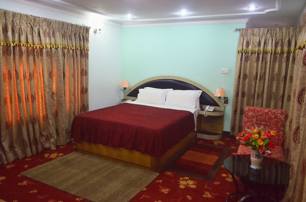 A cozy hotel room features a neatly made bed with red bedding, patterned curtains, and warm lighting, creating an inviting atmosphere ideal for travelers seeking comfort and relaxation.