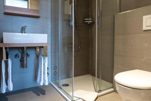 A modern bathroom featuring a sleek glass-enclosed shower, a minimalist sink with wooden accents, and a clean toilet, ideal for travelers seeking contemporary comfort in their accommodations.