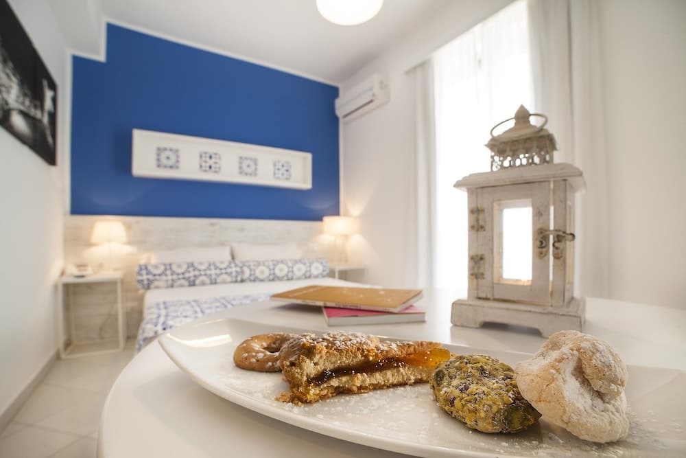A cozy bedroom with a blue accent wall and tiled headboard sets a serene mood, featuring a plate of assorted pastries on a table alongside a decorative lantern, ideal for travelers seeking a relaxing retreat with local culinary delights.