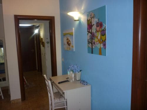A cozy apartment hallway features a vibrant blue wall adorned with colorful artwork, a small dining table set with fresh flowers, and warm lighting, creating an inviting atmosphere ideal for travelers seeking a comfortable stay.