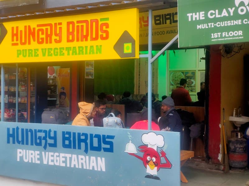 A bustling vegetarian eatery in McLeod Ganj, India, features vibrant signage and patrons enjoying meals, ideal for travelers seeking authentic local cuisine in a lively street-side setting.