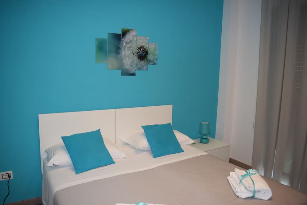 A serene hotel bedroom features a vibrant turquoise wall adorned with a dandelion artwork, complemented by cozy bedding and neatly folded towels, ideal for travelers seeking relaxation.