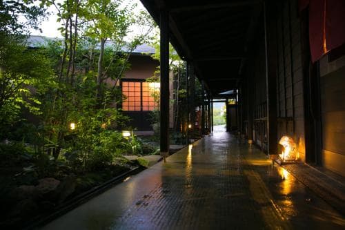 A serene evening at a traditional Japanese courtyard features a wet stone path illuminated by soft lanterns, surrounded by lush greenery, ideal for tranquil cultural exploration.