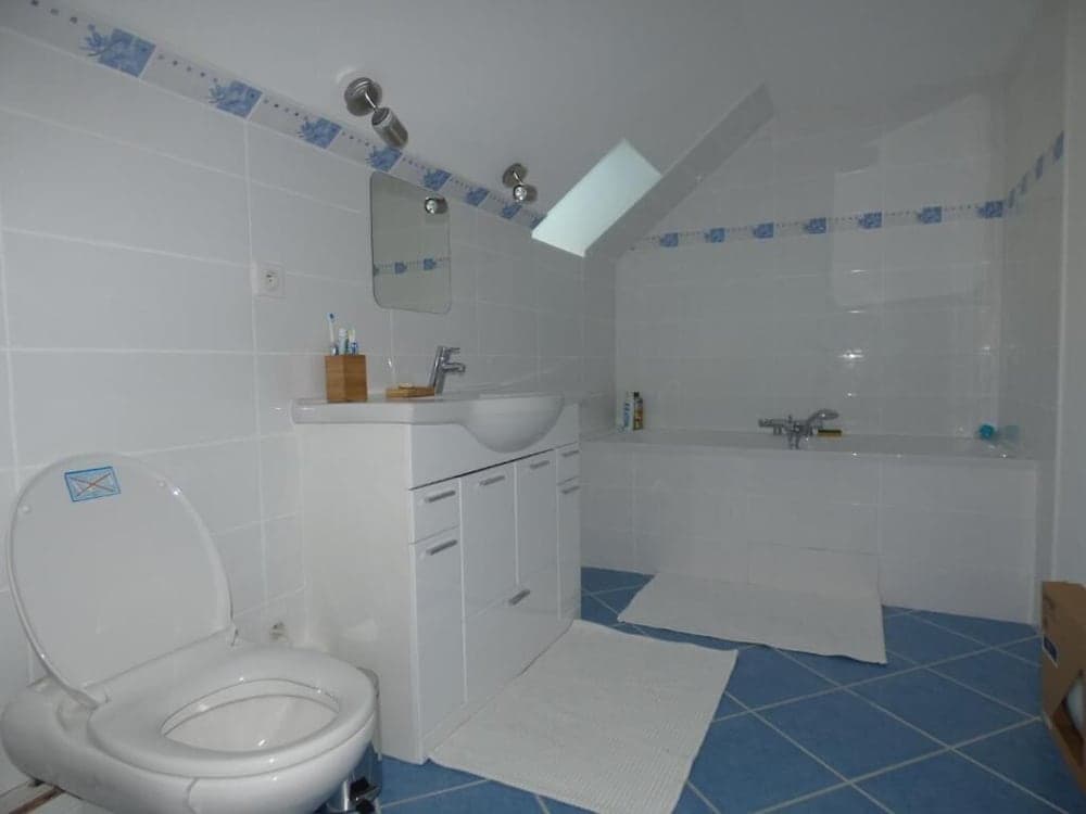 A cozy bathroom with white tiled walls, blue floor tiles, a skylight, and modern fixtures offers a clean and functional space ideal for travelers seeking comfort in accommodations.