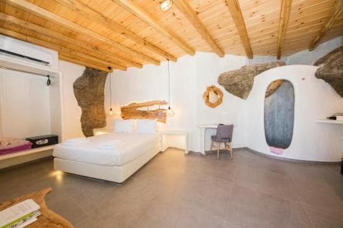A cozy cave-themed bedroom with exposed rock formations, wooden ceiling beams, and minimalist decor offers a unique and serene retreat for travelers seeking an unconventional lodging experience.