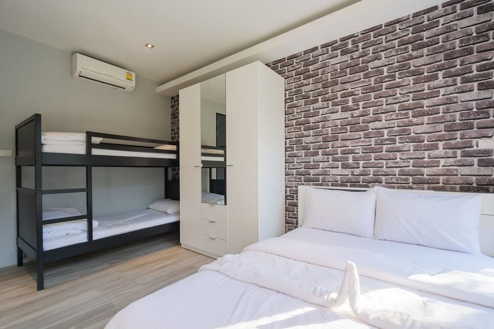 A cozy hostel room features a brick accent wall, bunk beds, a double bed with white linens, and modern furnishings, ideal for budget travelers seeking comfort and style.