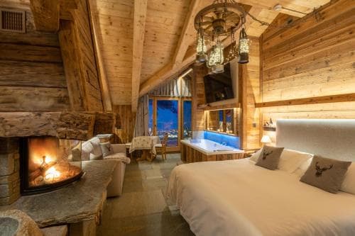 A cozy cabin-style bedroom with wooden interiors, a glowing fireplace, and a serene night view through large windows, perfect for a luxurious mountain retreat experience.