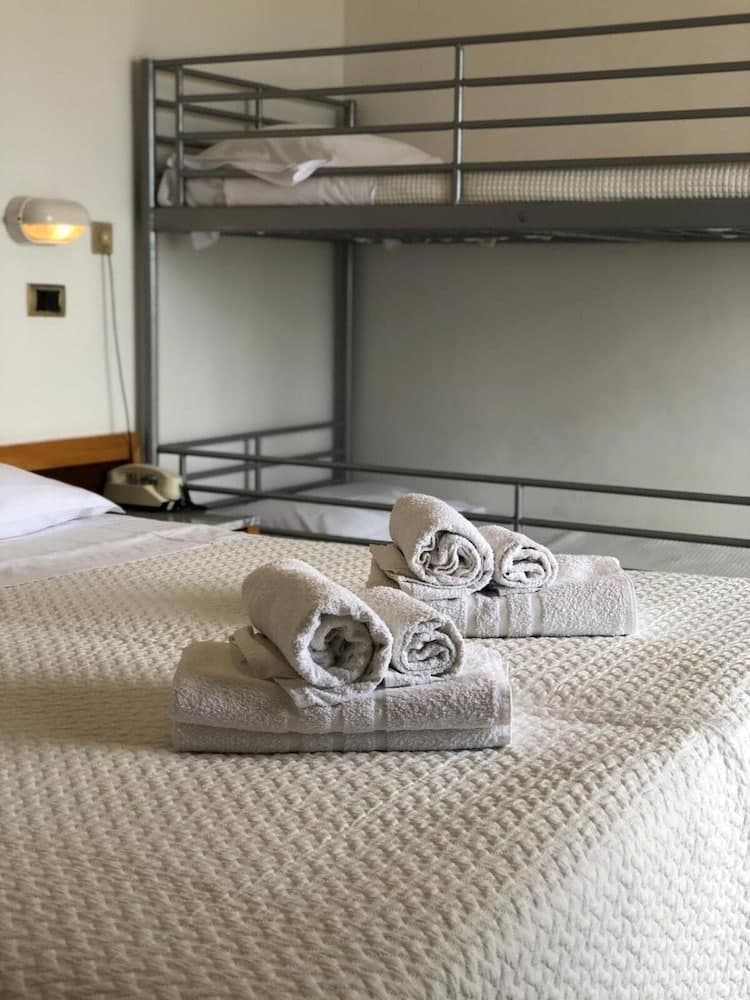 A cozy hostel room features neatly folded towels on a bed, a bunk bed in the background, and soft lighting, ideal for budget travelers seeking comfort.