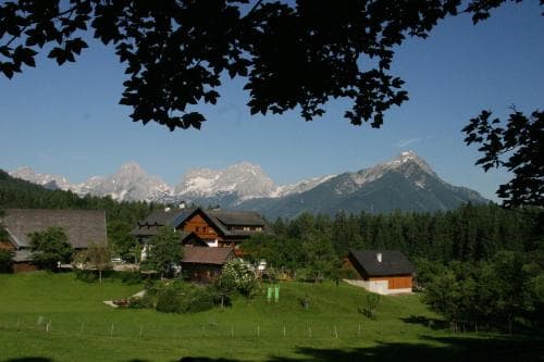 A serene mountain village with quaint wooden houses nestled in lush greenery under towering snow-capped peaks, perfect for tranquil alpine retreats.