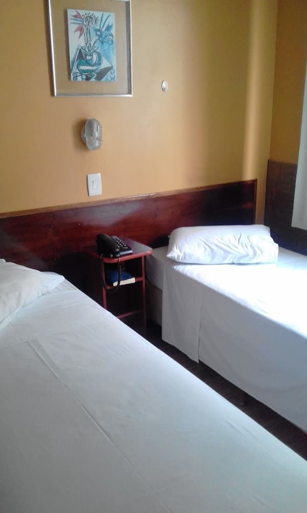 A cozy hotel room with two neatly made beds, a small wooden nightstand holding a telephone, and a vibrant wall art piece creates a welcoming atmosphere ideal for travelers seeking comfort and simplicity.