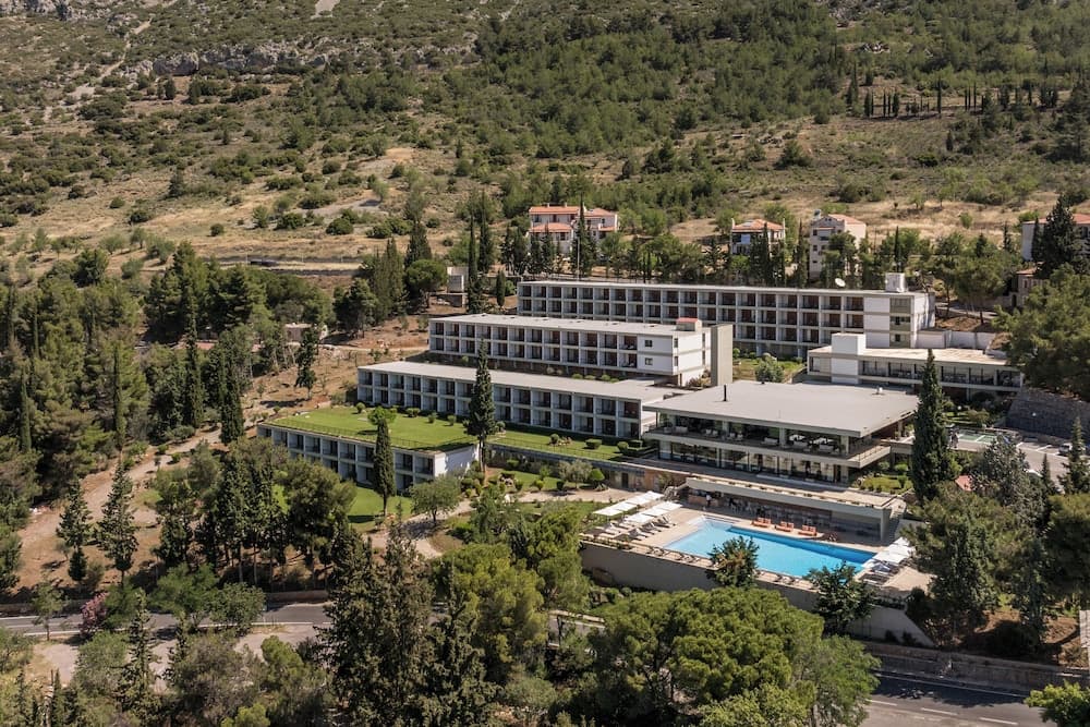 A serene resort nestled among lush greenery features modern buildings, a vibrant blue pool, and a tranquil atmosphere, ideal for travelers seeking relaxation in a picturesque natural setting.