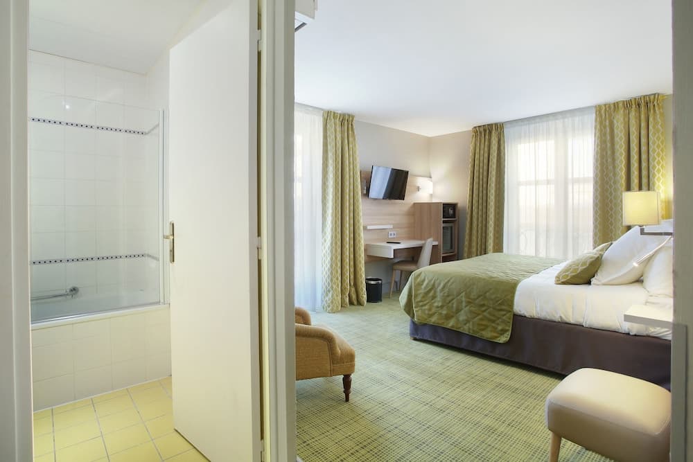 A cozy hotel room with green accents, a neatly made bed, desk area, and an adjacent bathroom featuring a bathtub, ideal for travelers seeking comfort and convenience.
