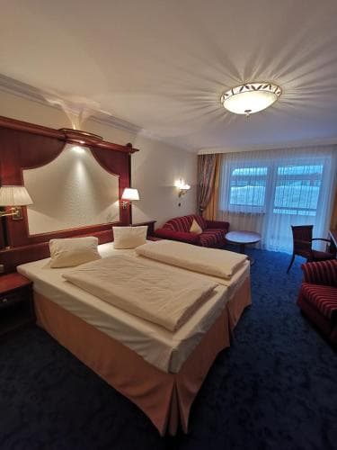 A cozy hotel room features a neatly made bed, plush seating by a curtained window, warm lighting, and a classic decor, ideal for travelers seeking comfort and relaxation.
