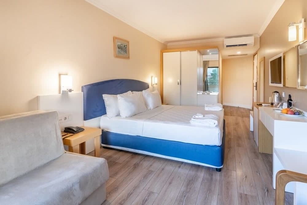 A cozy hotel room with a blue bed, wooden flooring, and modern amenities offers a comfortable stay for travelers seeking relaxation and convenience.