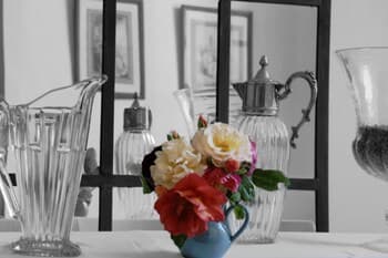 A serene indoor setting features a vibrant bouquet of roses in a blue pitcher surrounded by elegant glassware, evoking a cozy café ambiance ideal for a tranquil afternoon tea experience.