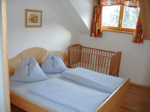 A cozy attic bedroom with wooden furnishings, a neatly made bed, a crib, and a window with colorful curtains offers a warm and inviting atmosphere ideal for family travelers seeking comfort in a quaint lodge setting.