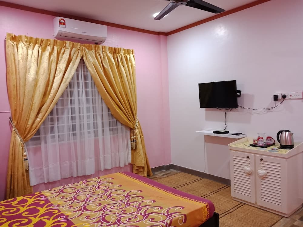 A cozy hotel room with pink walls, golden curtains, a vibrant bedspread, and modern amenities like a mounted TV and mini-fridge, ideal for travelers seeking comfort and convenience.
