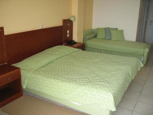 A cozy hotel room features two neatly made beds with green bedding, wooden nightstands, and a warm ambiance, ideal for travelers seeking comfort during their stay.