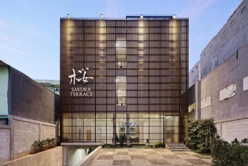 A modern urban hotel entrance featuring illuminated "Sakura Terrace" signage on a sleek, grid-patterned facade, ideal for travelers seeking stylish accommodations in a bustling cityscape.