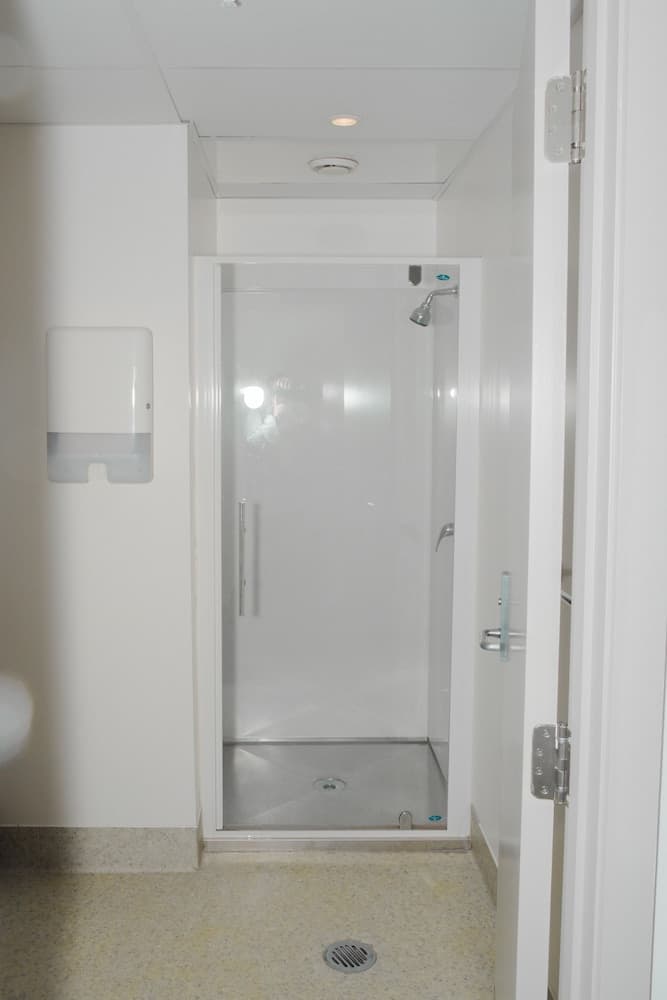 A modern, minimalist shower room with a glass-enclosed shower stall, sleek fixtures, and a wall-mounted dispenser creates a clean and functional space ideal for travelers seeking efficient accommodations.