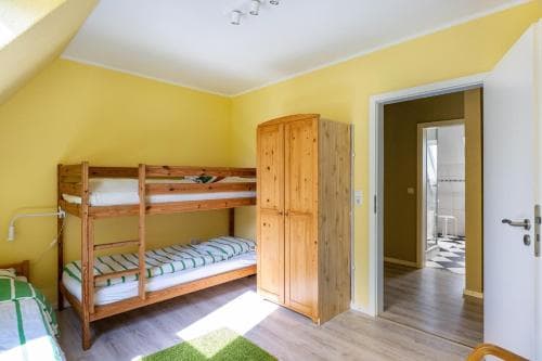 A cozy attic bedroom with yellow walls, wooden bunk beds, and a wardrobe, featuring natural light and an open doorway leading to a bathroom, ideal for budget-friendly family accommodations.