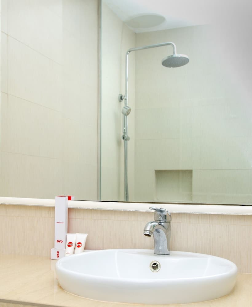 A clean, modern hotel bathroom features a sleek sink, chrome faucet, and shower setup reflected in a large mirror, complemented by neatly arranged toiletries, ideal for travelers seeking comfort and convenience.
