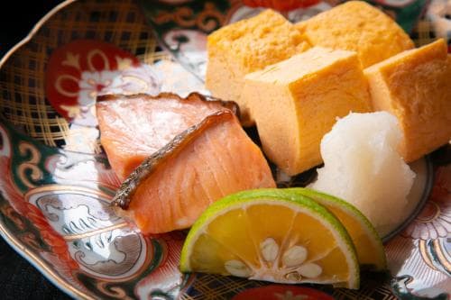 A beautifully arranged plate featuring salmon, tofu, and citrus slices on an ornate dish evokes a serene dining experience in a traditional Japanese restaurant, perfect for travelers seeking authentic culinary adventures.