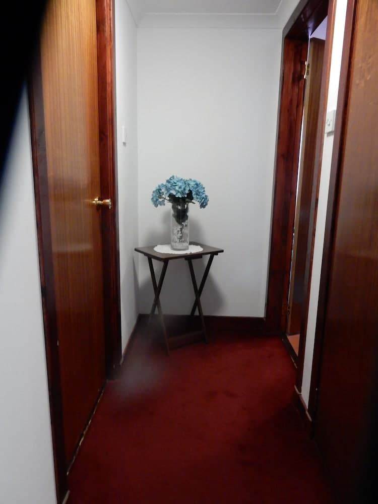 A cozy hotel hallway features a small table with blue hydrangeas in a vase, set against wooden doors and red carpeting, creating a welcoming atmosphere for travelers seeking comfort.