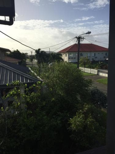 A serene suburban neighborhood view featuring lush greenery, residential houses with red roofs, and a clear sky, ideal for travelers seeking a peaceful retreat or exploring local living environments.