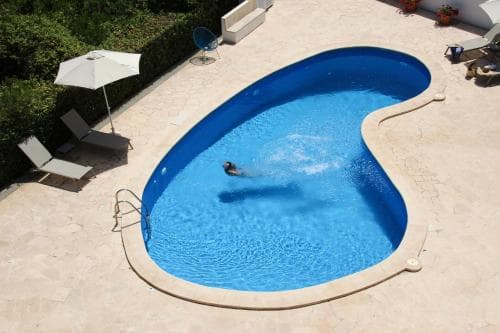 A serene private pool area features a swimmer enjoying the vibrant blue water, surrounded by lounge chairs, an umbrella, and lush greenery, ideal for a relaxing vacation retreat.