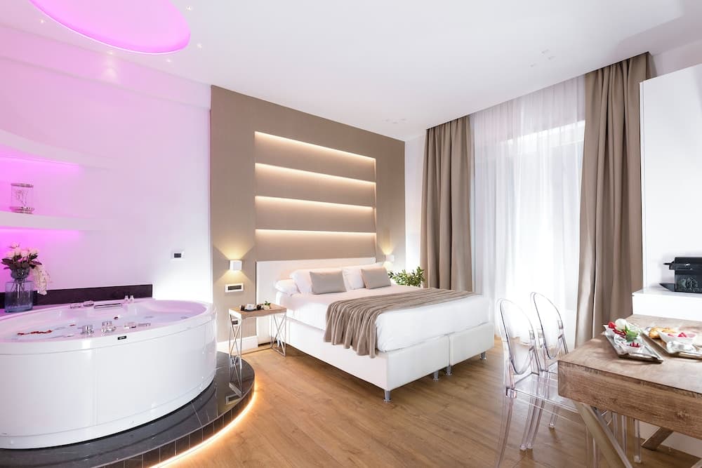 A luxurious hotel suite features a cozy bed with soft lighting, a modern bathtub with ambient purple glow, and a dining area by large windows, ideal for a romantic getaway or a relaxing retreat.