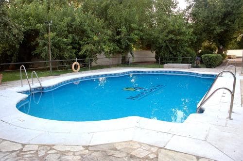A serene outdoor swimming pool surrounded by lush greenery offers a tranquil retreat, featuring metal railings and a lifebuoy, ideal for vacation relaxation.