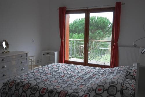 A cozy bedroom with a patterned bedspread overlooks a serene balcony surrounded by lush greenery, ideal for travelers seeking relaxation in a tranquil retreat.