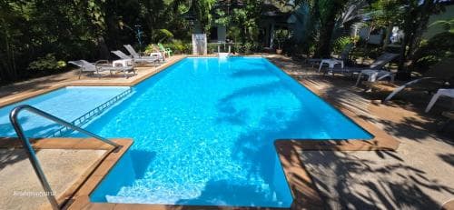 A serene tropical resort pool surrounded by lush greenery, featuring lounge chairs and a wooden deck, ideal for relaxing vacations and leisurely escapes.
