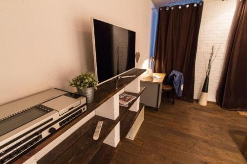 A cozy living room with a retro-inspired entertainment setup featuring a vintage stereo system, flat-screen TV, and wooden flooring, ideal for travelers seeking a nostalgic and comfortable stay.