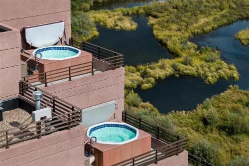 A serene rooftop retreat features two private hot tubs overlooking lush greenery and a tranquil river, ideal for a relaxing getaway or romantic escape.