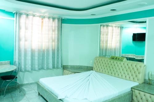 A cozy hotel room features a neatly made bed with a tufted headboard, sheer curtains over large windows, and a modern desk area, creating a serene and inviting atmosphere ideal for travelers seeking comfort and relaxation.