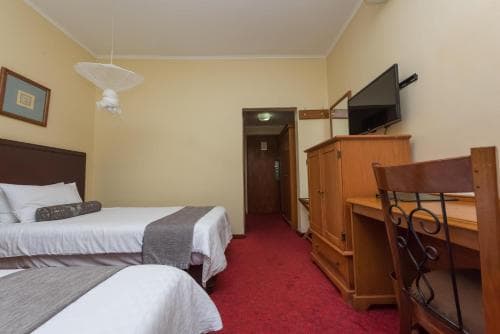 A cozy hotel room features two neatly made beds, a wooden desk with a chair, a mounted TV, and warm yellow walls, ideal for travelers seeking comfort and functionality in a budget-friendly accommodation.