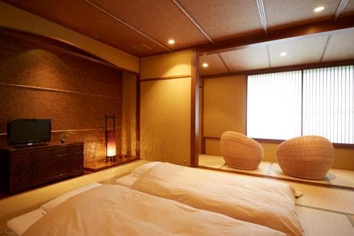 A serene Japanese-style room features tatami flooring, futon beds, woven stools, and soft lighting, ideal for travelers seeking a tranquil and authentic accommodation experience.