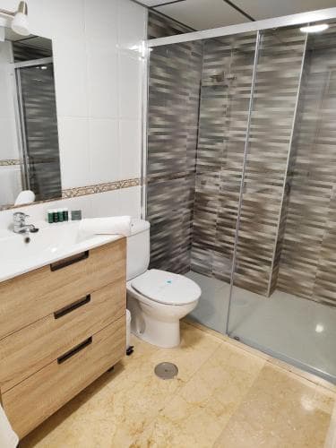 A modern bathroom with a sleek glass shower enclosure, wooden vanity, and tiled flooring offers a clean and inviting space ideal for travelers seeking comfort and style in their accommodations.