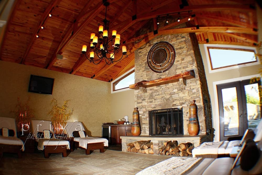 A cozy cabin-style living room with a stone fireplace, wooden beams, and a warm chandelier creates an inviting atmosphere perfect for a relaxing getaway.