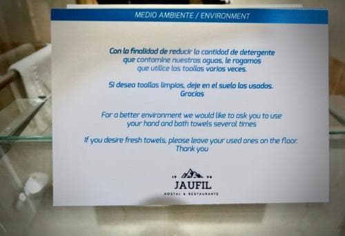 A sign in a hotel bathroom promotes environmental conservation by encouraging guests to reuse towels, featuring bilingual text and a logo, ideal for eco-conscious travelers seeking sustainable accommodations.