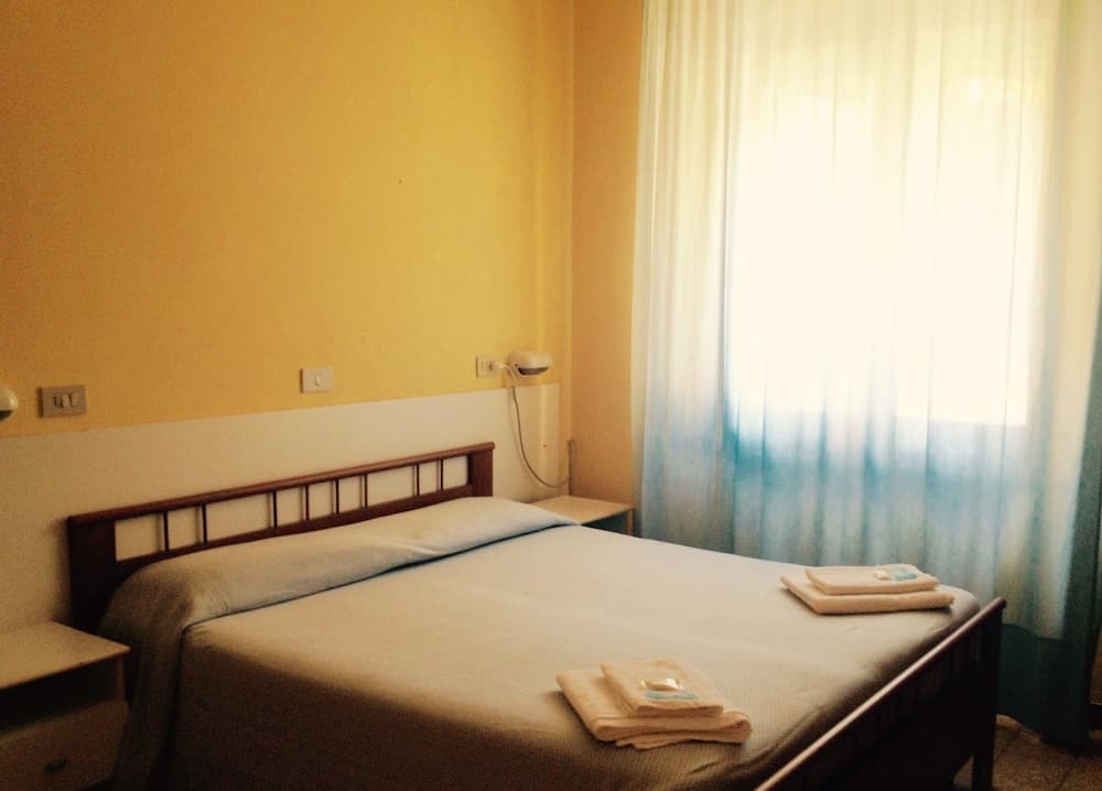 A cozy hotel room with a neatly made bed, yellow walls, soft lighting through sheer curtains, and folded towels on the bed invites travelers seeking a comfortable and tranquil stay.