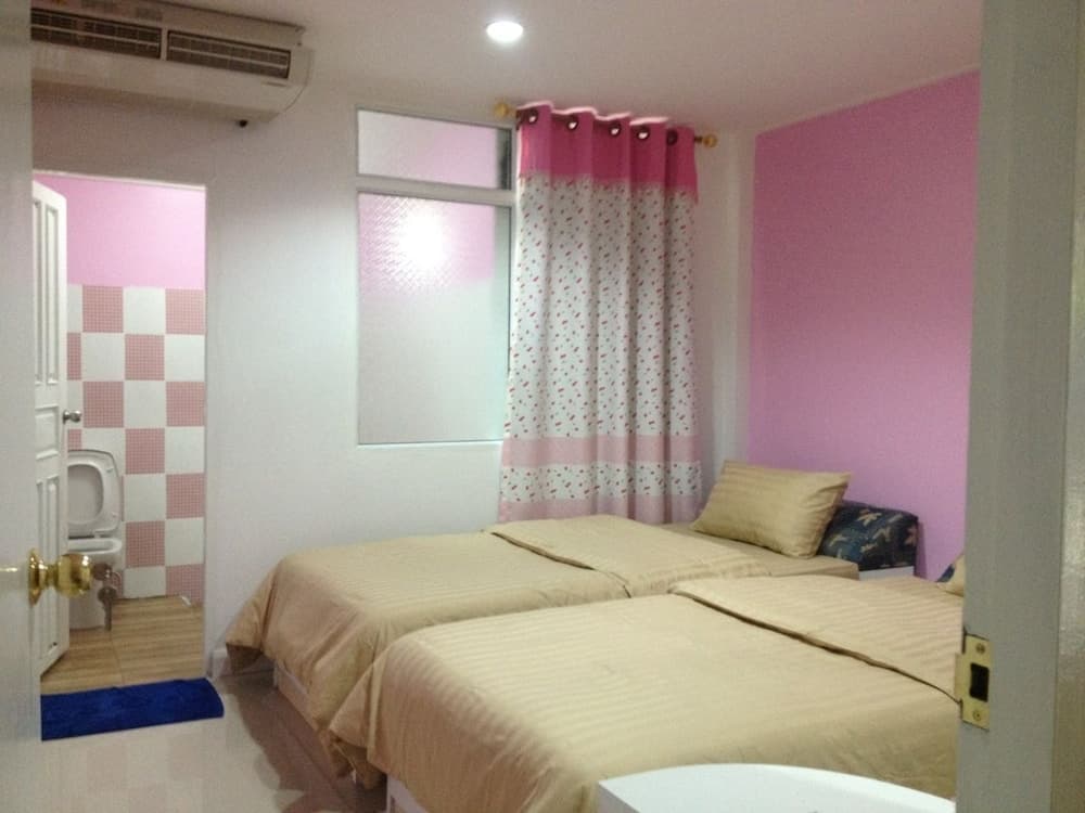 A cozy hotel room with twin beds, pink walls, patterned curtains, and an adjacent bathroom offers a comfortable stay for travelers seeking a charming and inviting accommodation.
