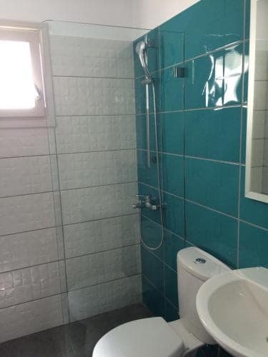 A modern bathroom with turquoise and white tiled walls, featuring a glass shower enclosure, toilet, sink, and natural light from a small window, ideal for travelers seeking clean and stylish accommodations.