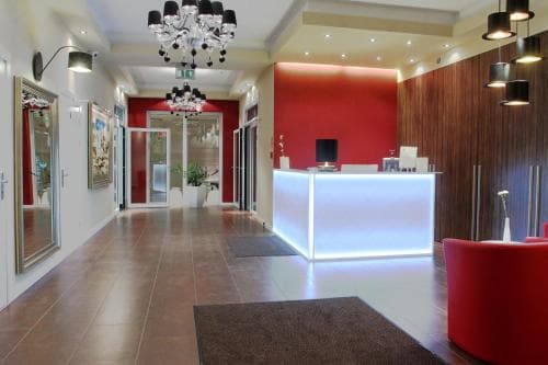A modern hotel lobby features sleek tiled floors, vibrant red accents, contemporary chandeliers, and a glowing reception desk, creating an inviting atmosphere ideal for travelers seeking comfort and style.
