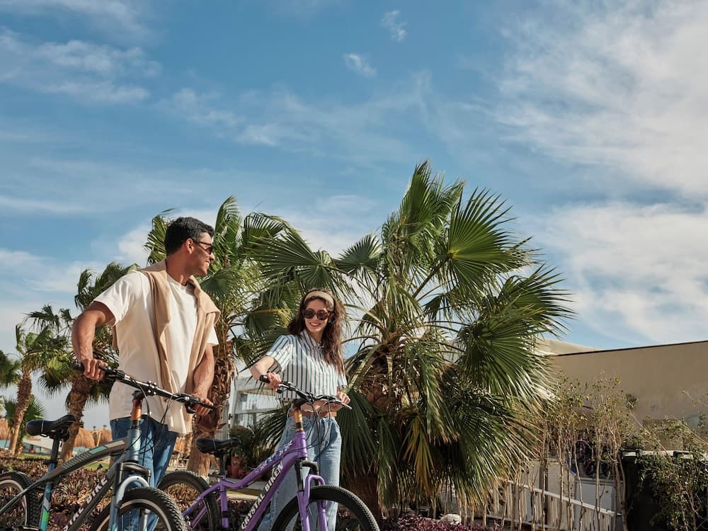 A cheerful couple enjoys a sunny day on bicycles amidst lush palm trees, perfect for a tropical vacation adventure.